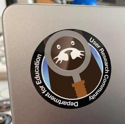 Photo of a sticker on a laptop computer. The sticker shows a cartoon otter holding a magnifying glass